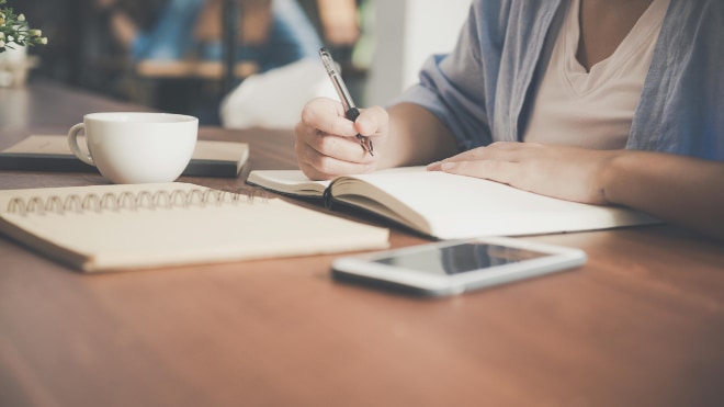 A person studying at a desk with pad and paper.