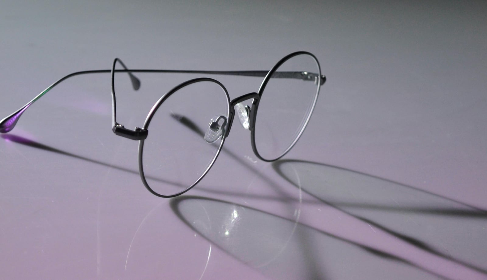A pair of glasses cast a shadow across a flat surface.