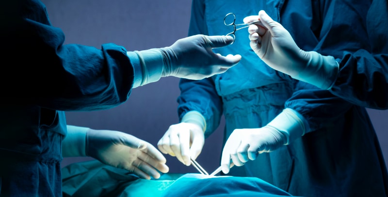 A patient being operated on in surgery, as a surgeon is passed a pair of surgical scissors.