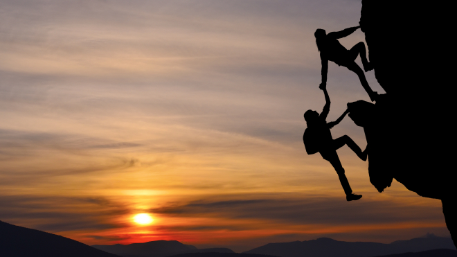 Two rock climbers helping each other up a mountain