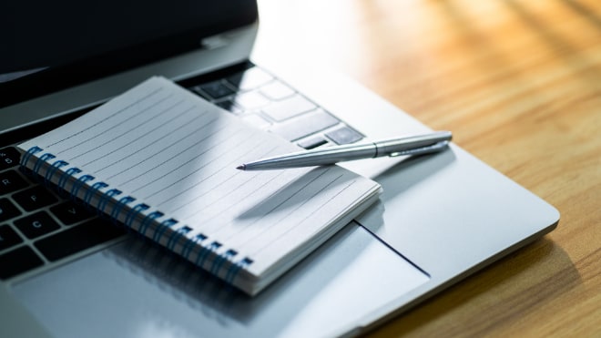 A pen and notepad, resting on a laptop.