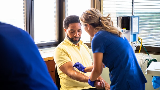 A man sitting whilst a nurse prepares his arm for an injection.